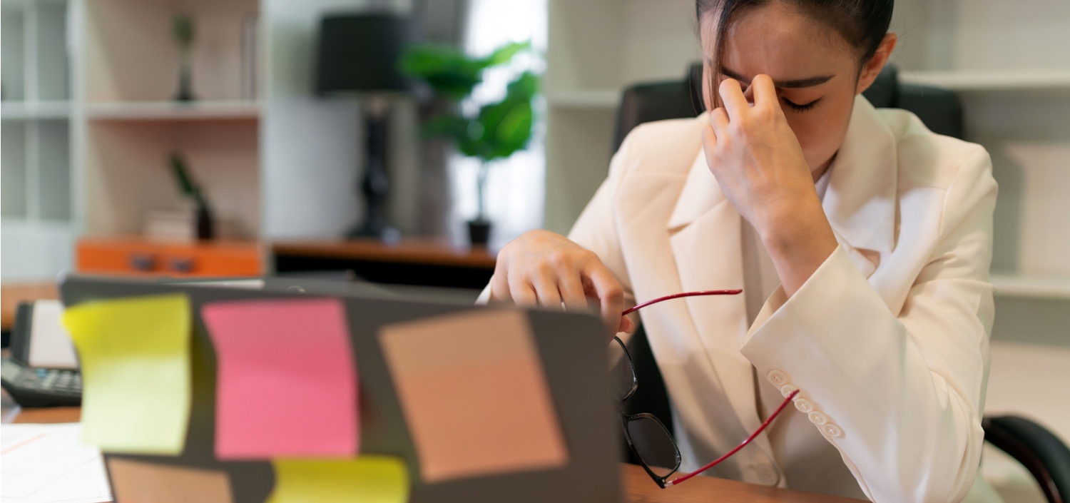 stressed businesswoman at laptop with lots of sticky notes, whose compliance engagement is running her